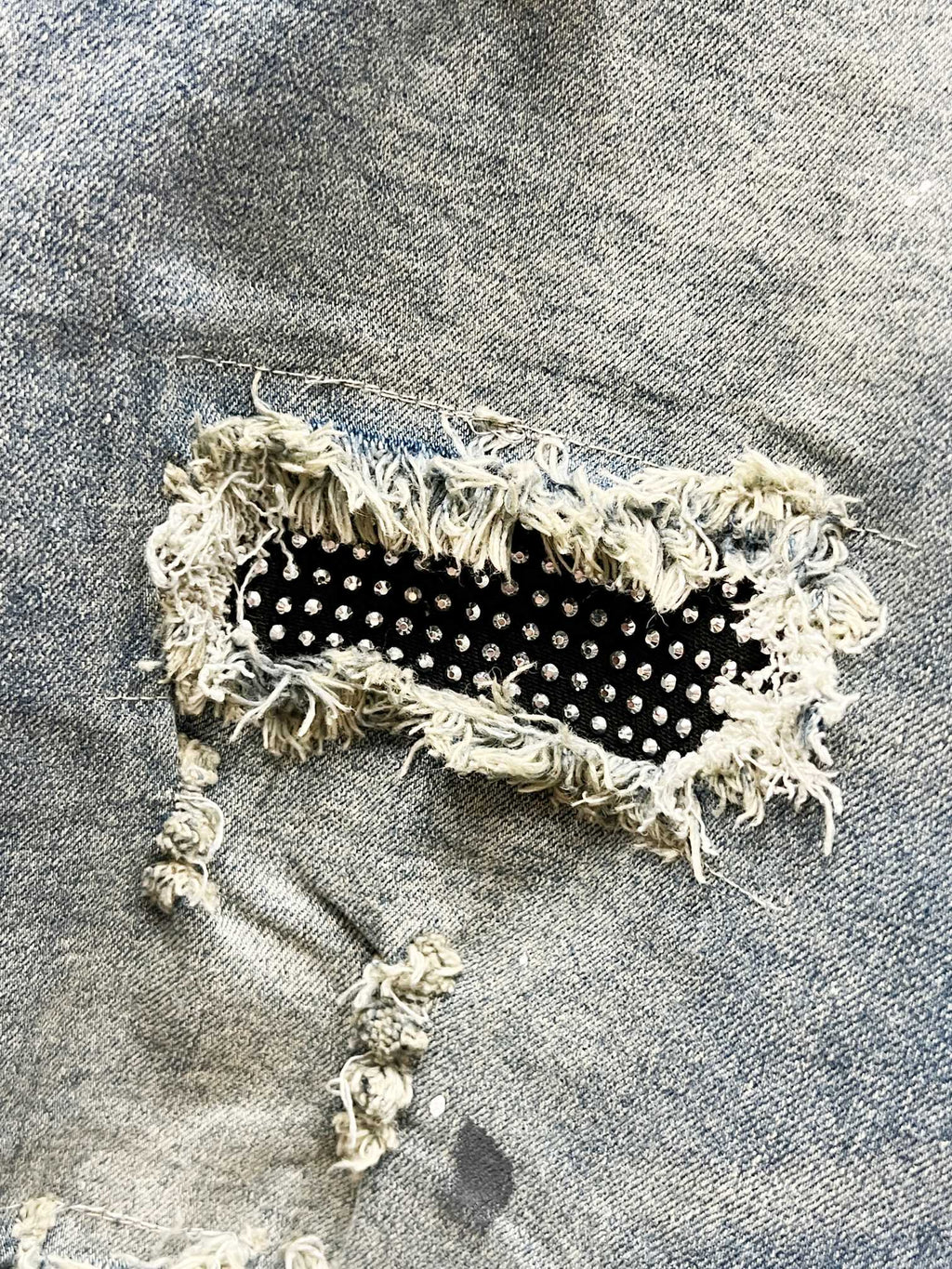 Distressed denim jeans patch with black fabric and small studs, frayed edges