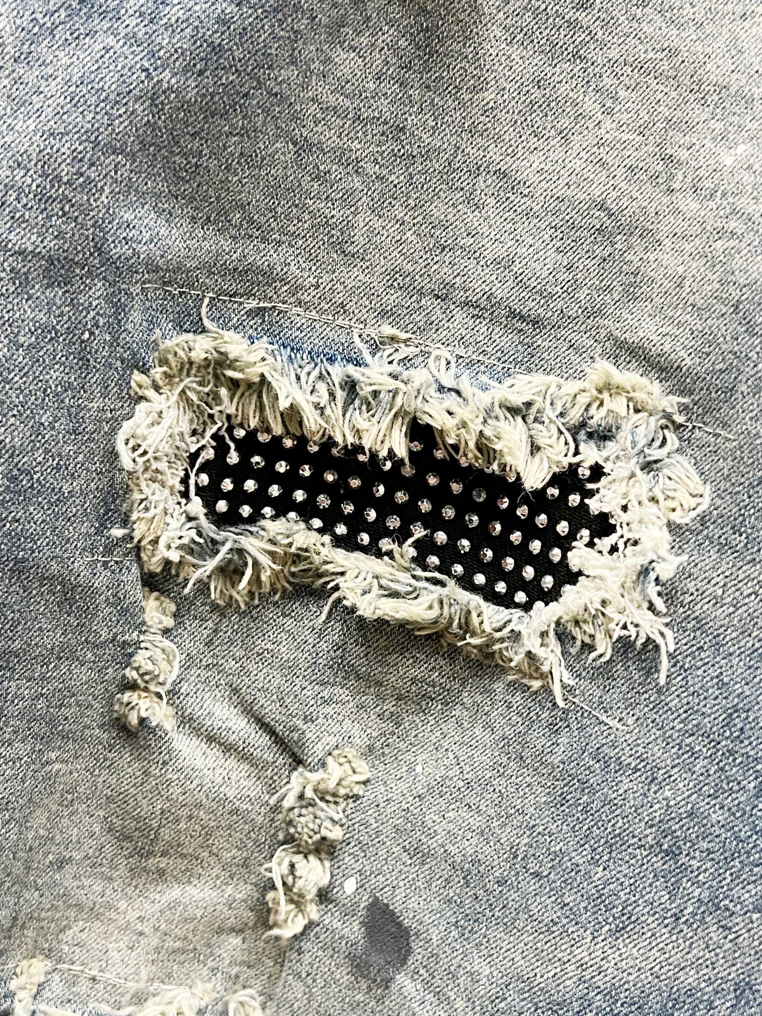 Distressed denim jeans patch with black fabric and small studs, frayed edges
