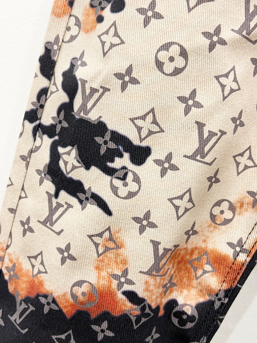 Monogram print fabric with beige base and dark accents plus orange abstract patches