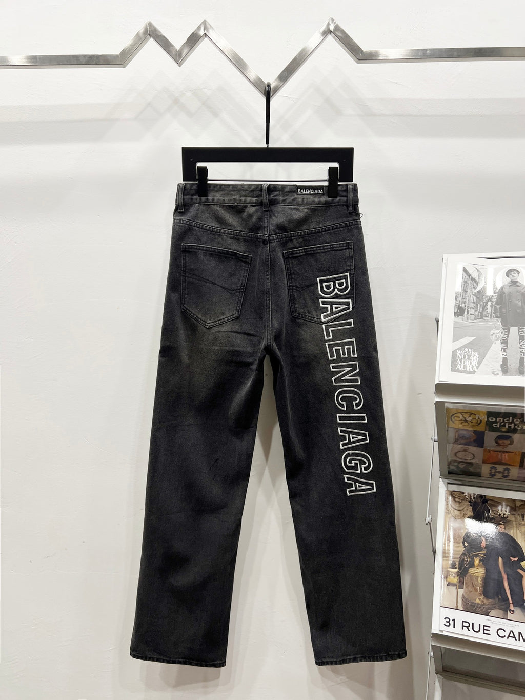 Dark denim pants on hanger with Balenciaga vertical text logo on right side