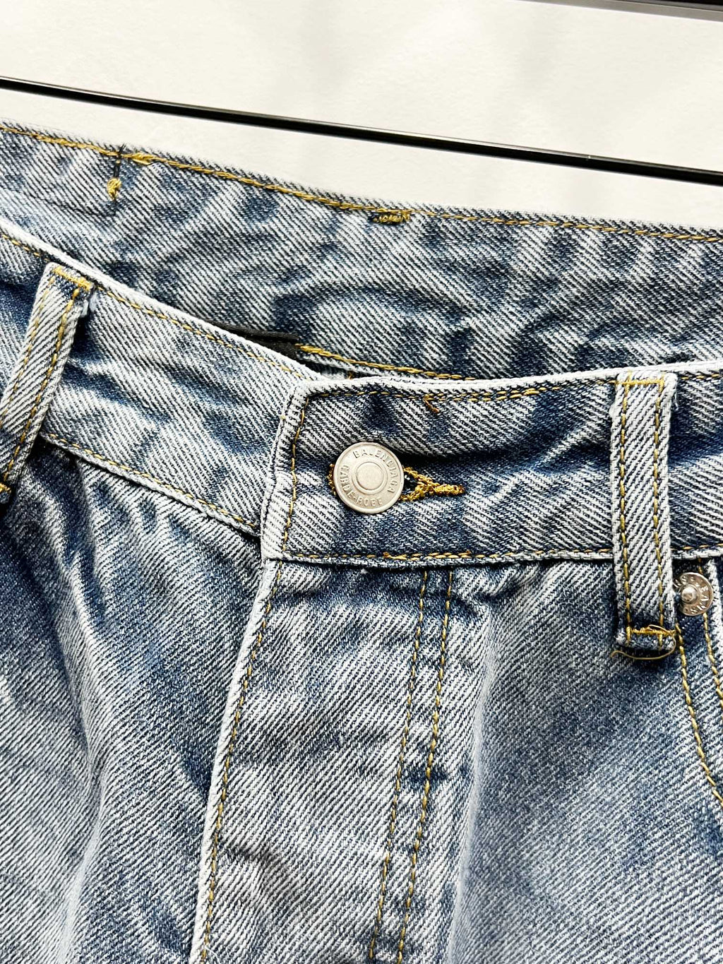 Light blue denim waistband close-up with metal button and belt loops