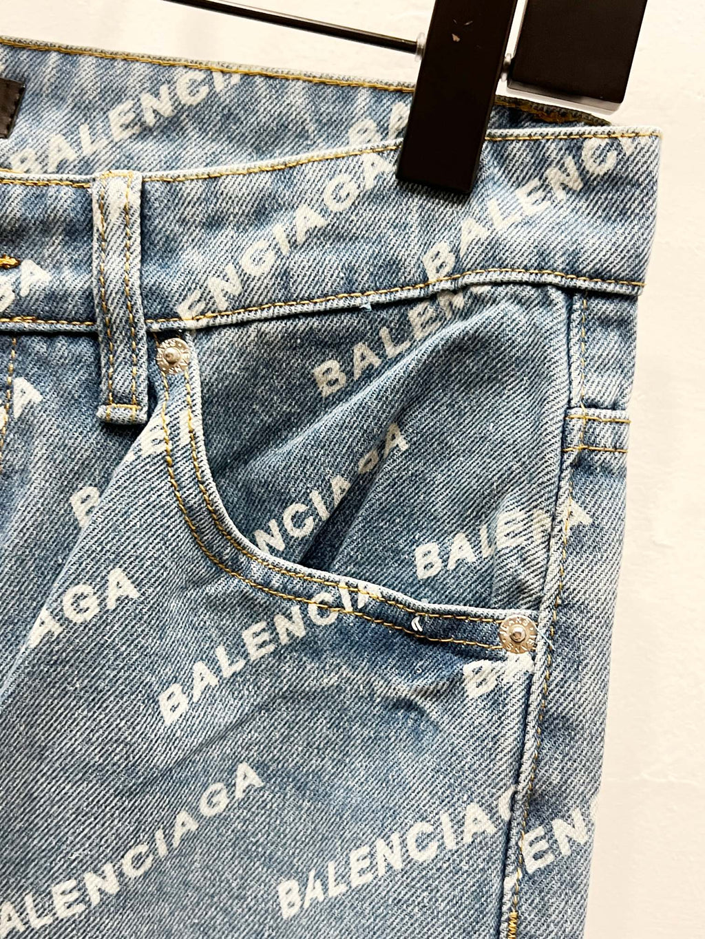 Front jean pocket close-up with logo print, metal button, and stitched seams