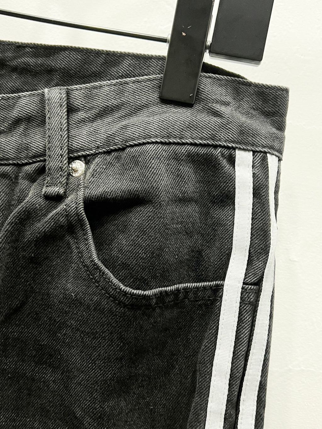 Black denim pants waistband with front button, belt loops, and vertical side stripe