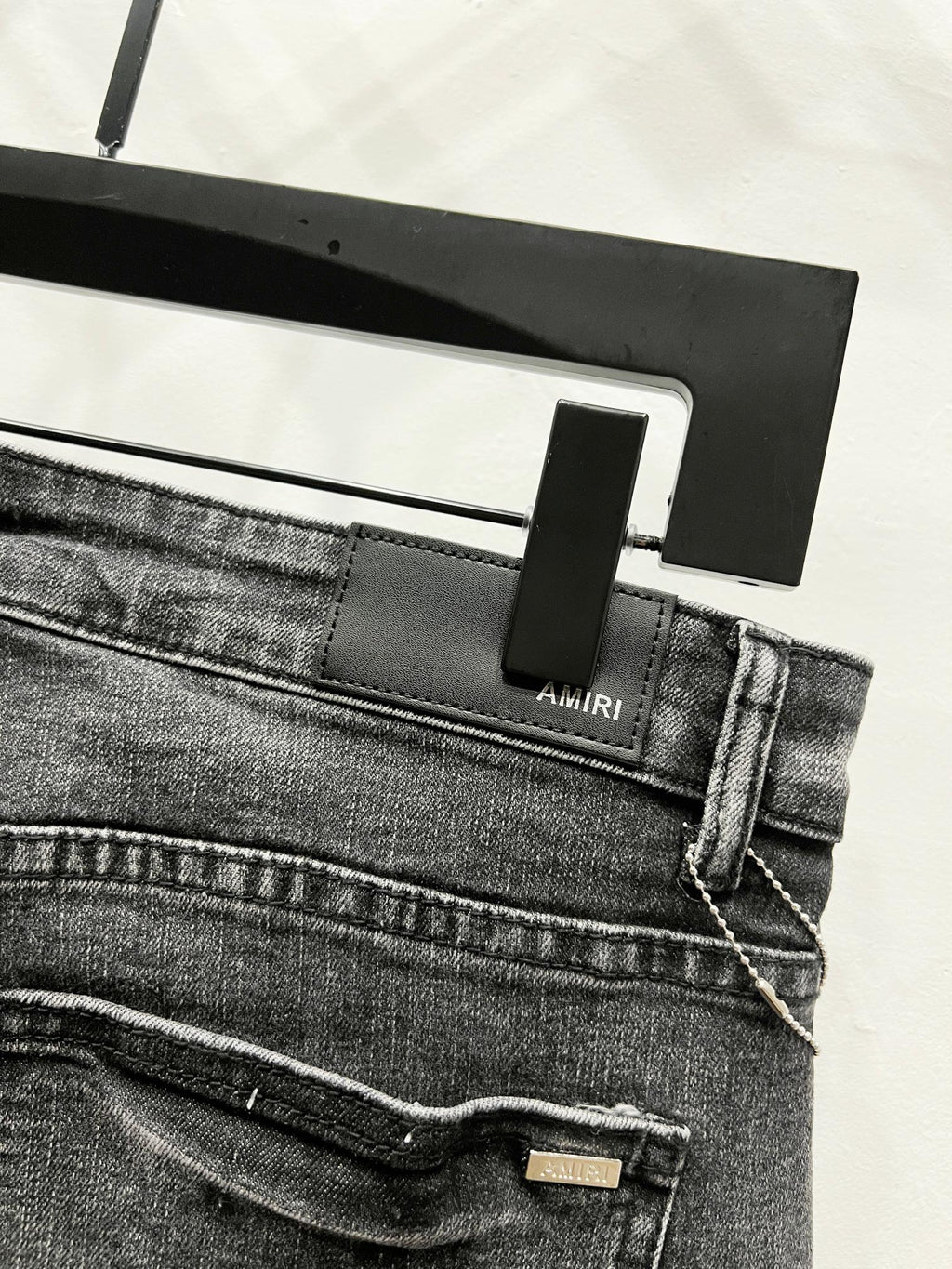 Black denim pants waistband with AMIRI label and belt loops, front seam detail