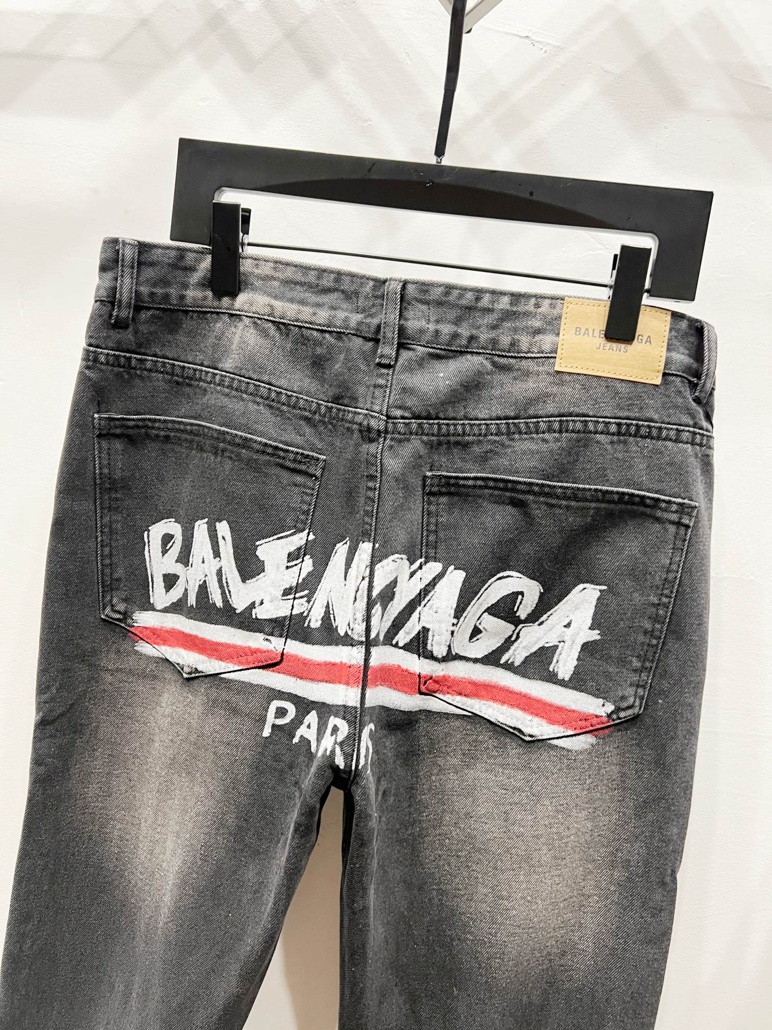 Grey-wash denim pants with Balenciaga Paris logo and red stripe, front close-up