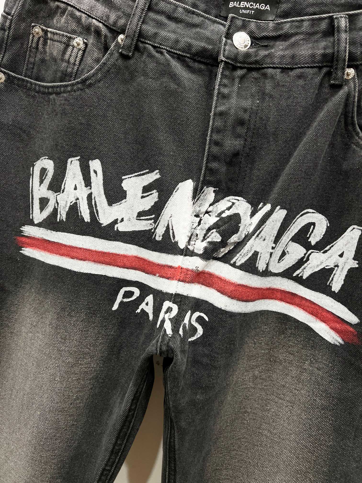 Black denim pants with Balenciaga graphic and red stripe, front close-up