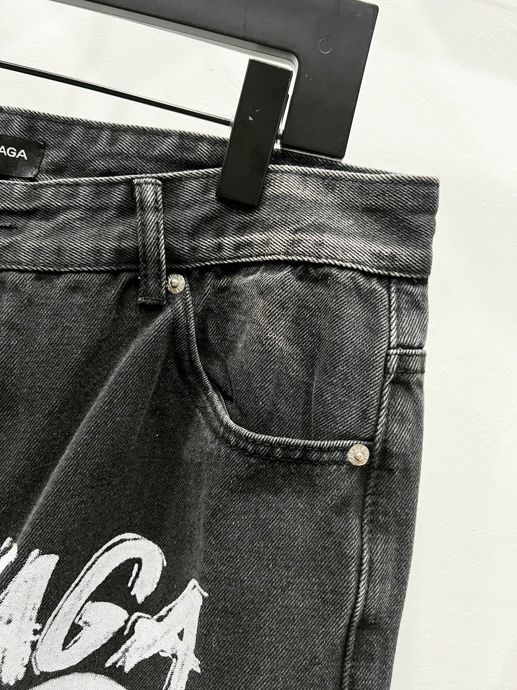 Black denim pants waistband with belt loops, button closure, and front pocket