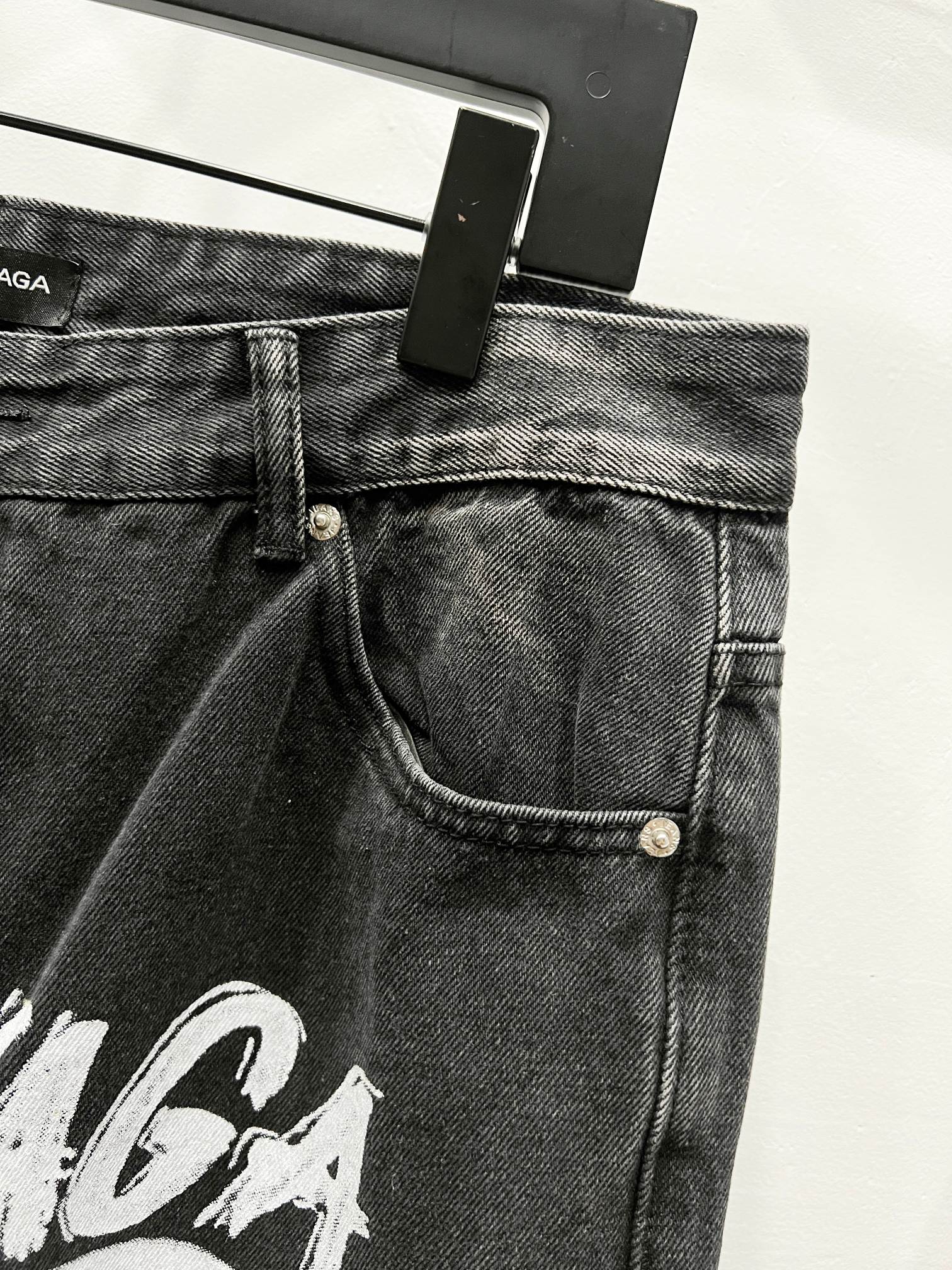 Black denim pants waistband with belt loops, button closure, and front pocket