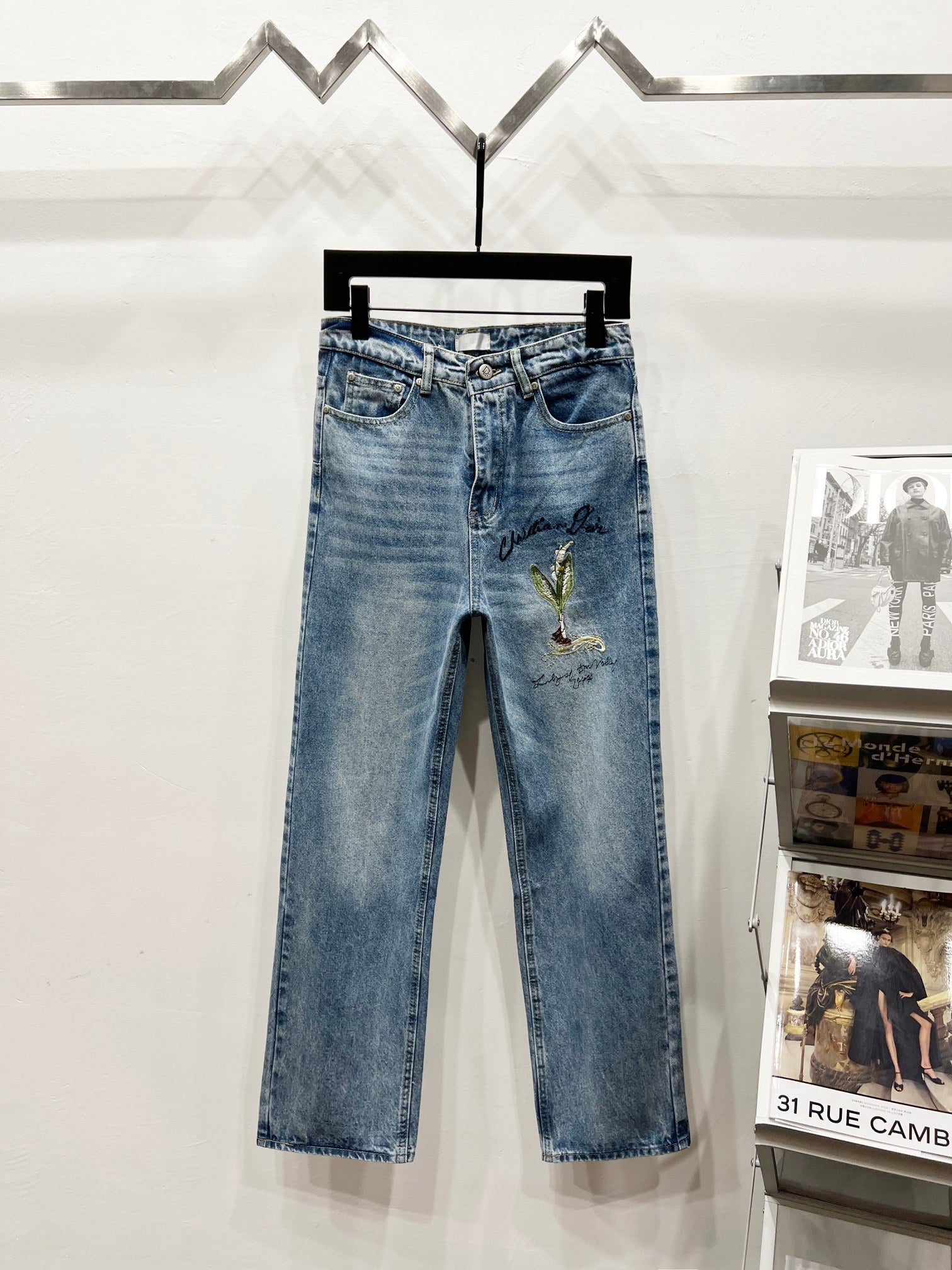 Light-wash denim pants with green-gold floral embroidery on one thigh