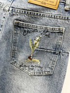 Light-wash denim pocket with green-gold floral crest embroidery