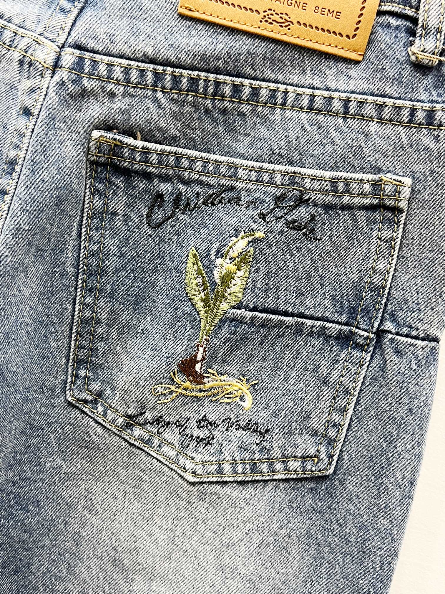 Light-wash denim pocket with green-gold floral crest embroidery
