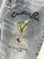 Light-wash denim thigh with green-gold floral embroidery and cursive text