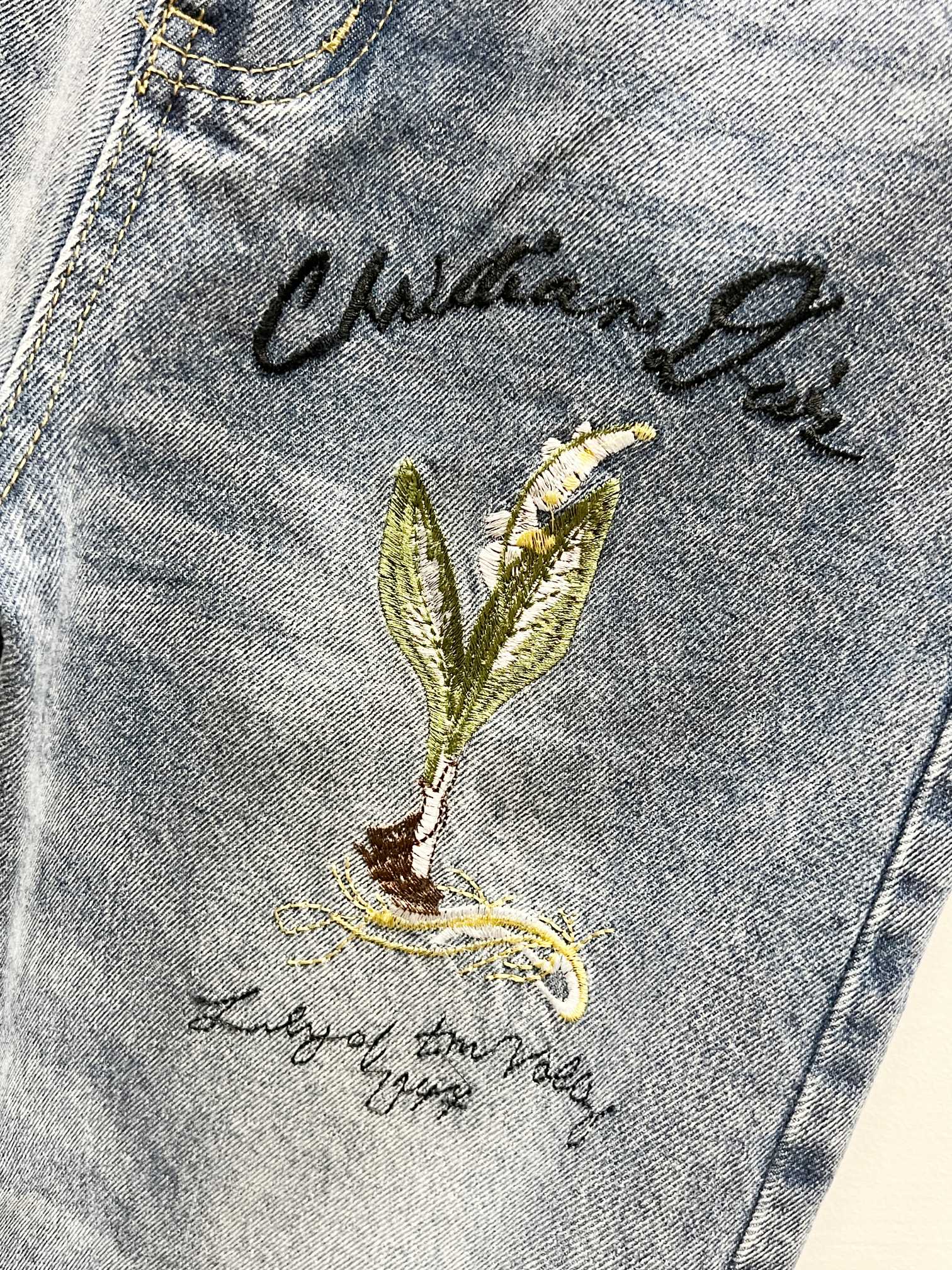 Light-wash denim thigh with green-gold floral embroidery and cursive text
