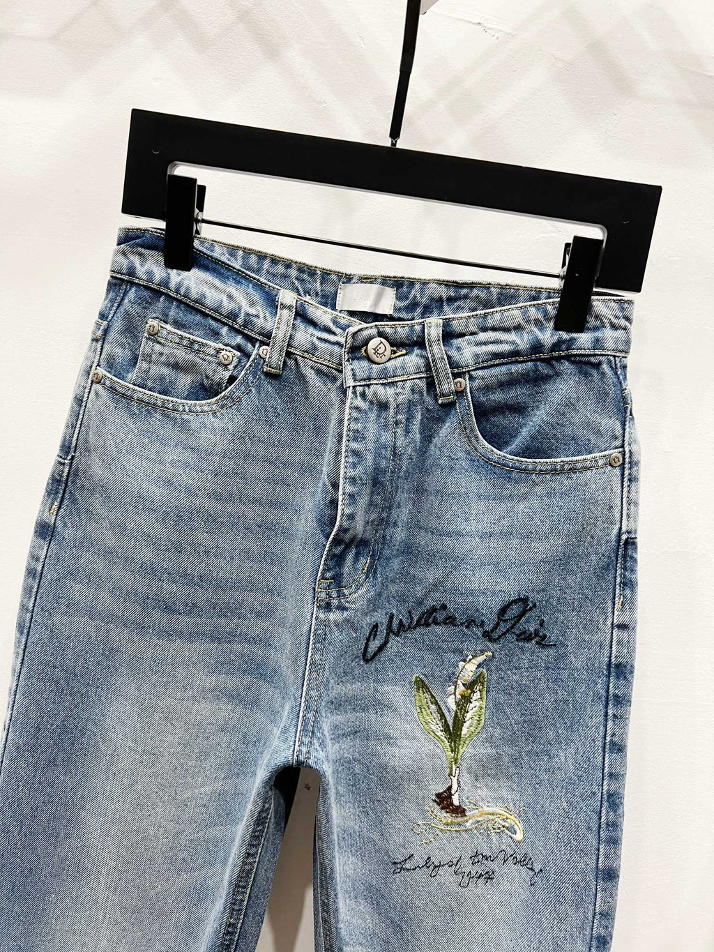 Light-wash denim pants with green-gold floral embroidery and button waist