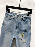 Light-wash denim pants with green-gold floral embroidery and button waist