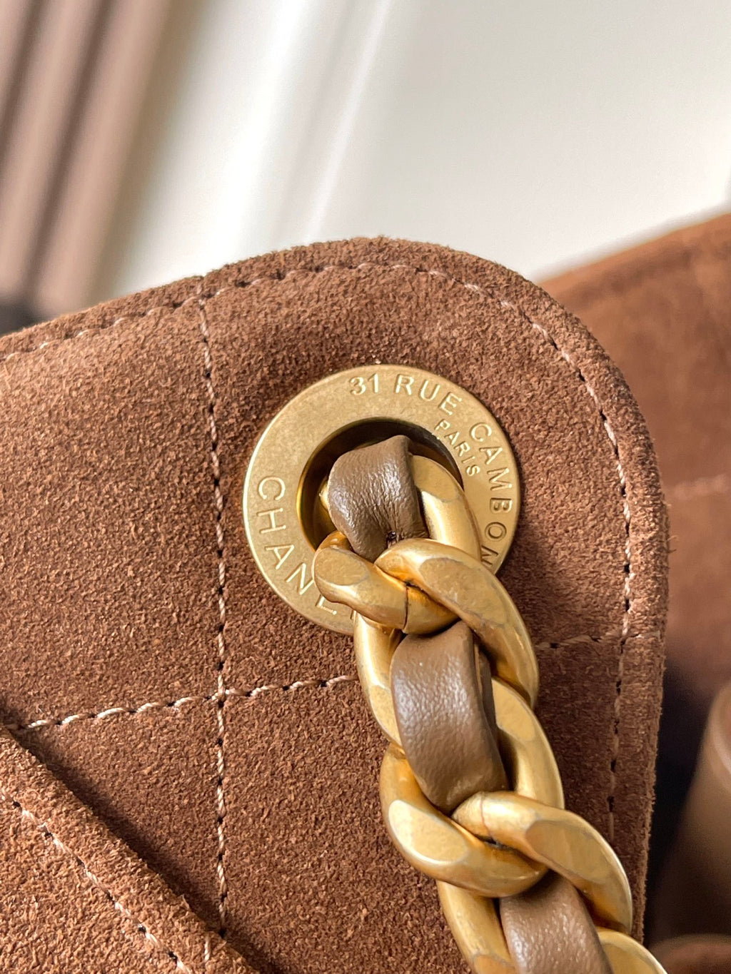 Round gold logo hardware with linked chain on tan-brown suede bag