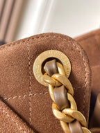 Round gold logo hardware with linked chain on tan-brown suede bag