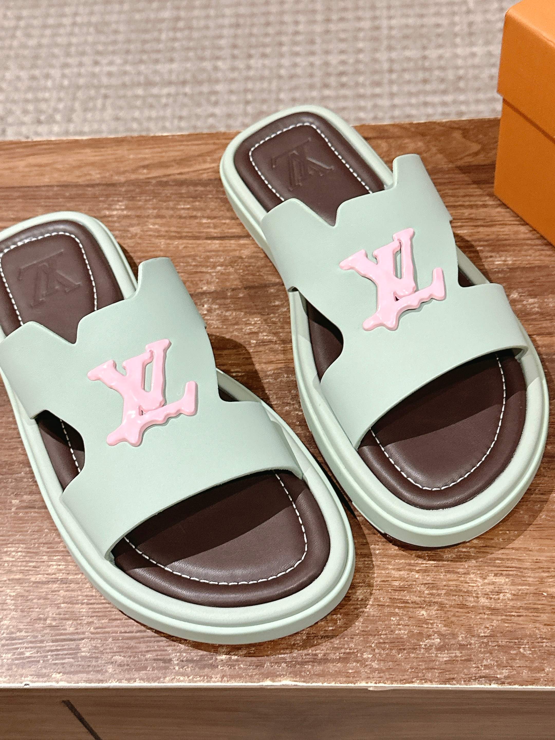 Two mint green slide sandals with pink LV emblems and brown interior footbeds