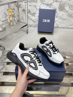 White Dior lace-up sneakers with black chunky soles, hand holding pair on box
