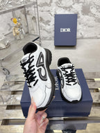 White Dior lace-up sneakers with black chunky soles, pair held above blue box