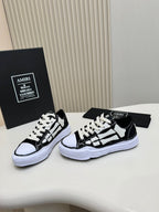 Two black and white low-top sneakers side by side, lace-up front and thick white sole