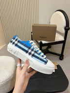 Burberry low-top sneaker held up, blue plaid with white laces and rubber sole