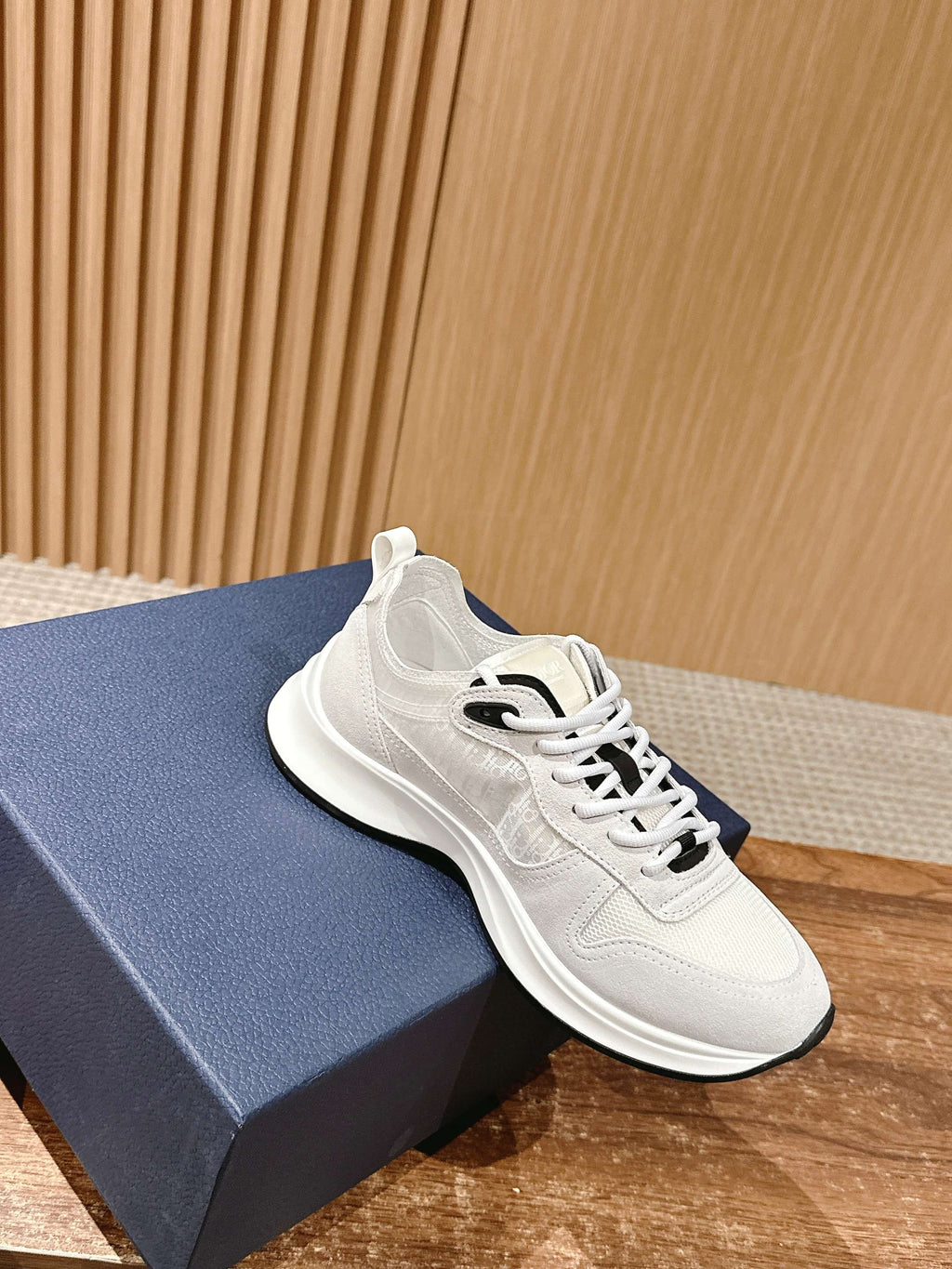White Dior sneakers on blue shoebox, lace-up with black accent