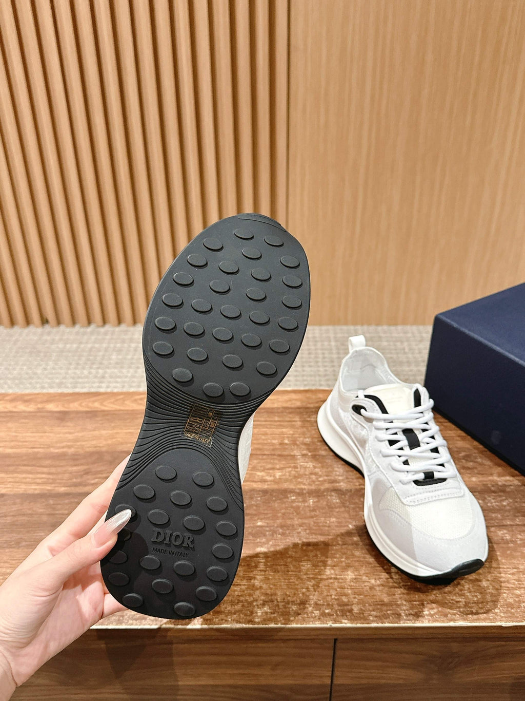 Black Dior sneaker outsole with tread pattern, white shoe shown beside box