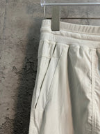 White cargo pants with pleated front, flap pocket, and drawstring at side