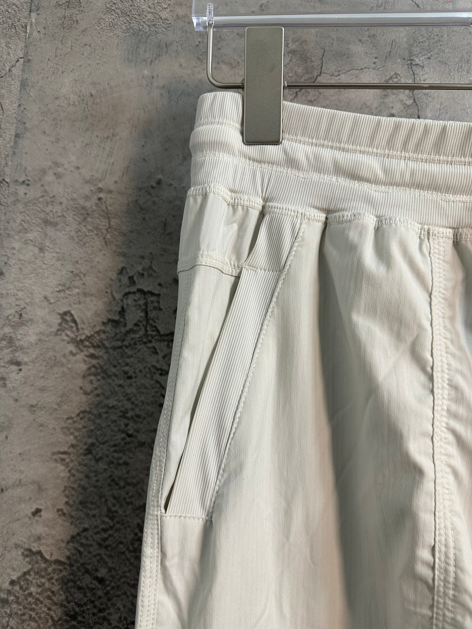 White cargo pants with pleated front, flap pocket, and drawstring at side