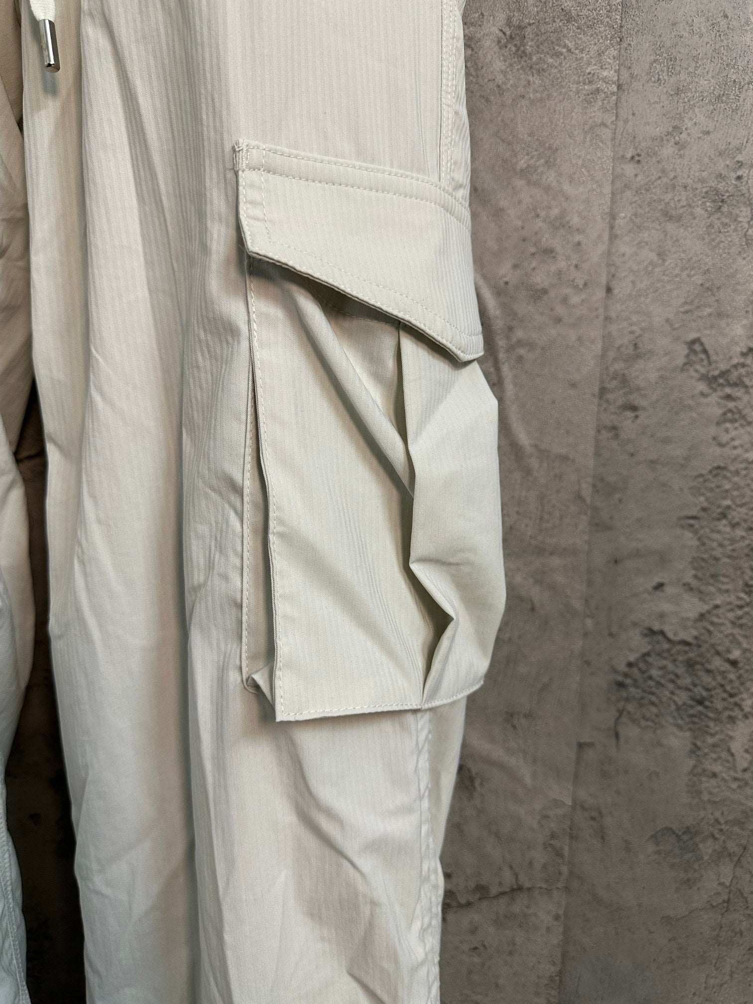 White cargo pants leg with flap pocket detail and vertical seam stitching