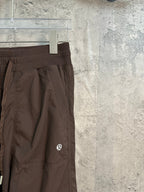Dark brown cargo pants side view with large pocket detail and small logo patch