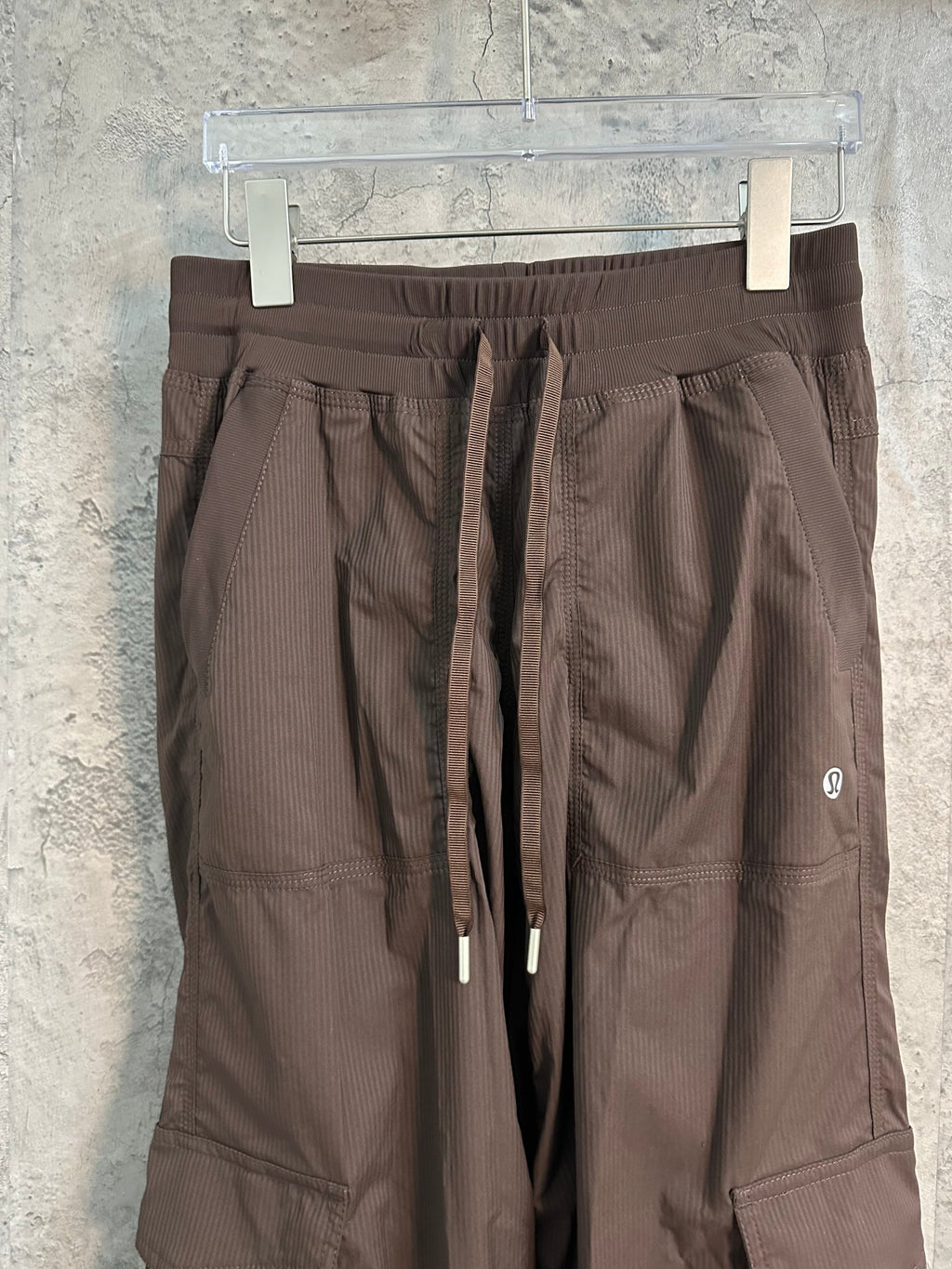 Dark brown cargo pants close-up showing waistband, drawstring ties, and side pockets