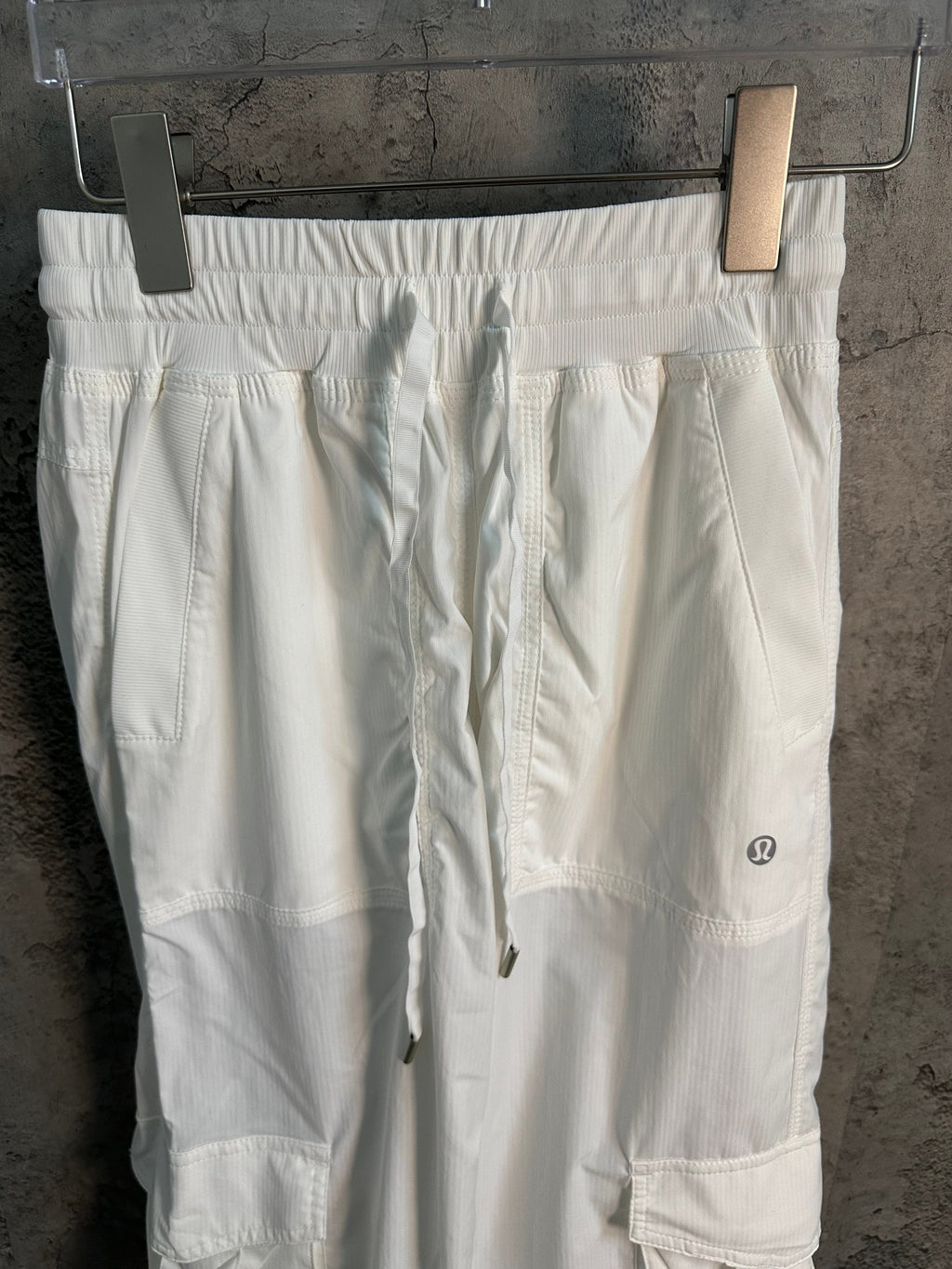 White cargo pants with elastic waistband, drawcord, and side pockets on thigh