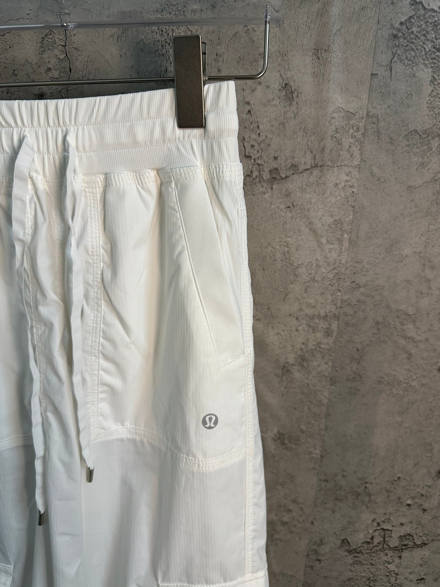 White cargo pants with side seams and small logo patch, close-up