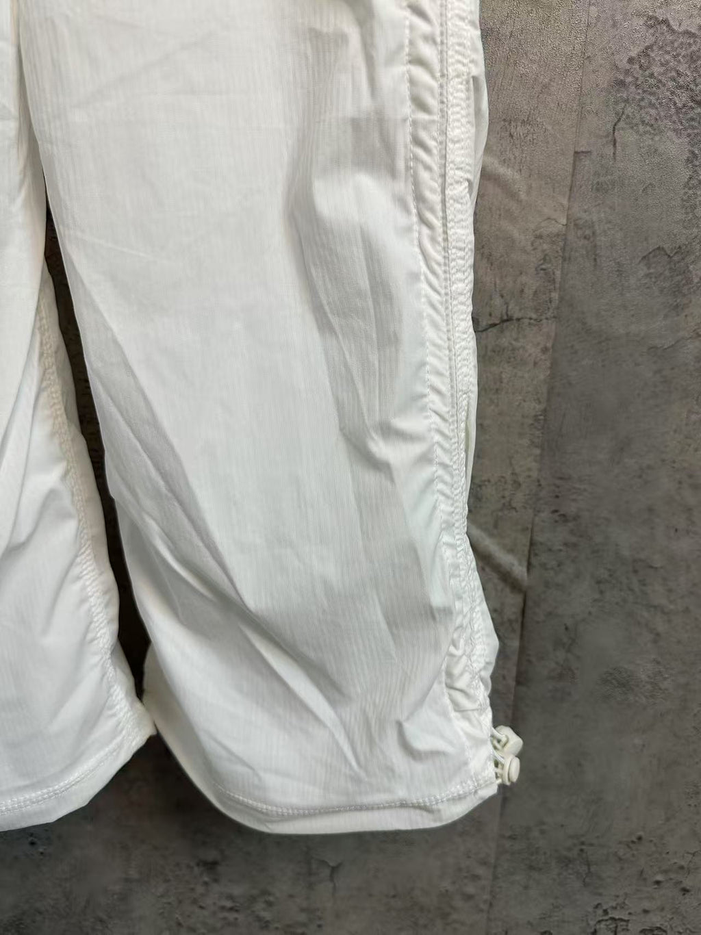White cargo pants with leg seam stitching and small fabric pull-tab at hem