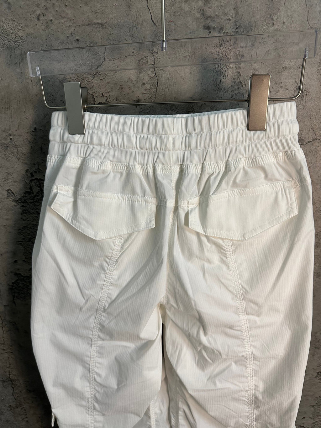 White cargo pants with elastic waistband and large front pockets, back view