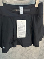 Black athletic skort with waistband tab and front pleats, hanging with tags