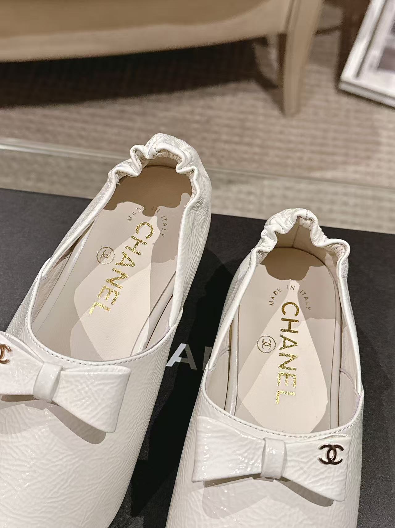Close-up of white pointed-toe flats with bow strap and Chanel branding on insole