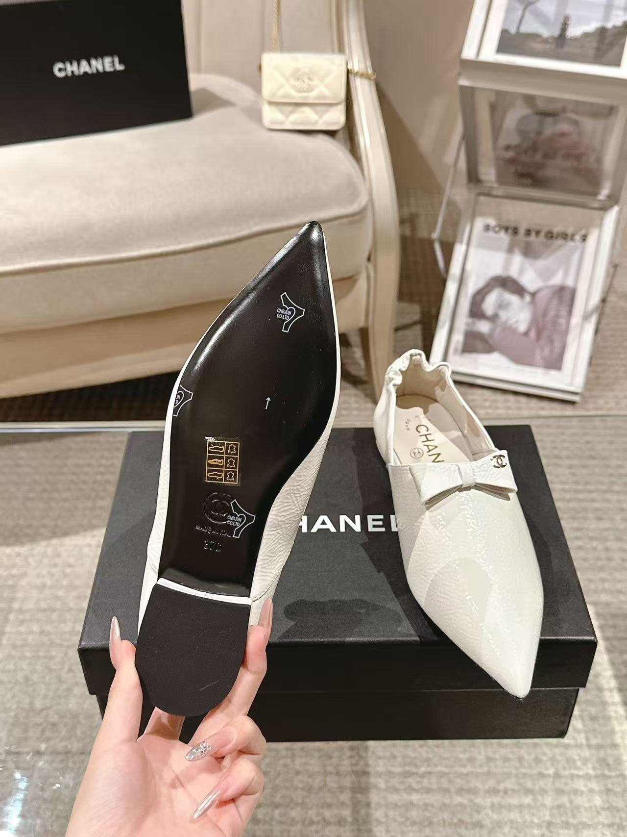 White pointed-toe flat with bow strap, showing black sole with logo graphics