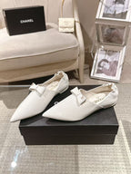 White leather pointed-toe flats with bow strap, shown on black display box