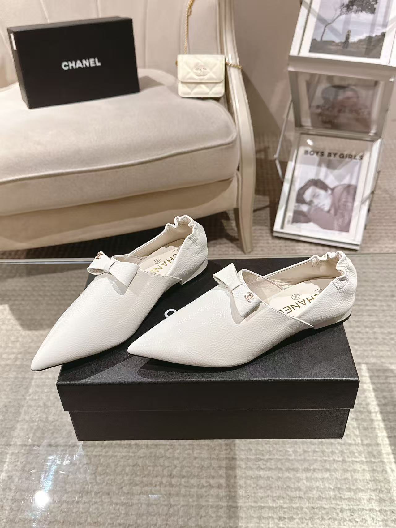 White leather pointed-toe flats with bow strap, shown on black display box