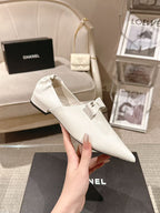 White pointed-toe flat with bow strap and low block heel, held in hand