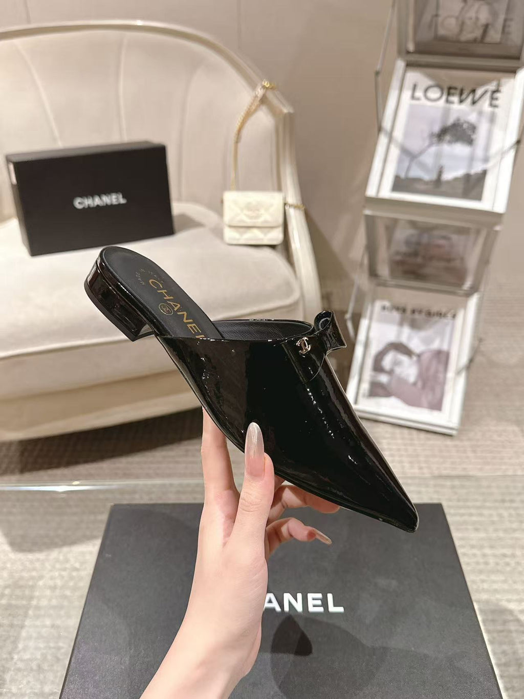 Women’s glossy black patent pointed-toe mule held in hand over a CHANEL box