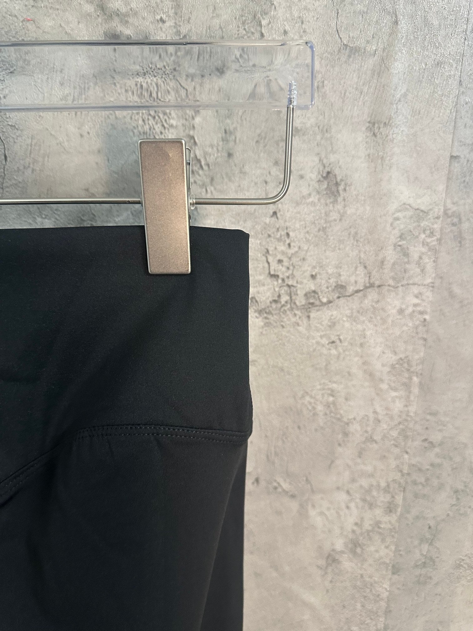 Black pants side view with smooth waistband and stitched hem.