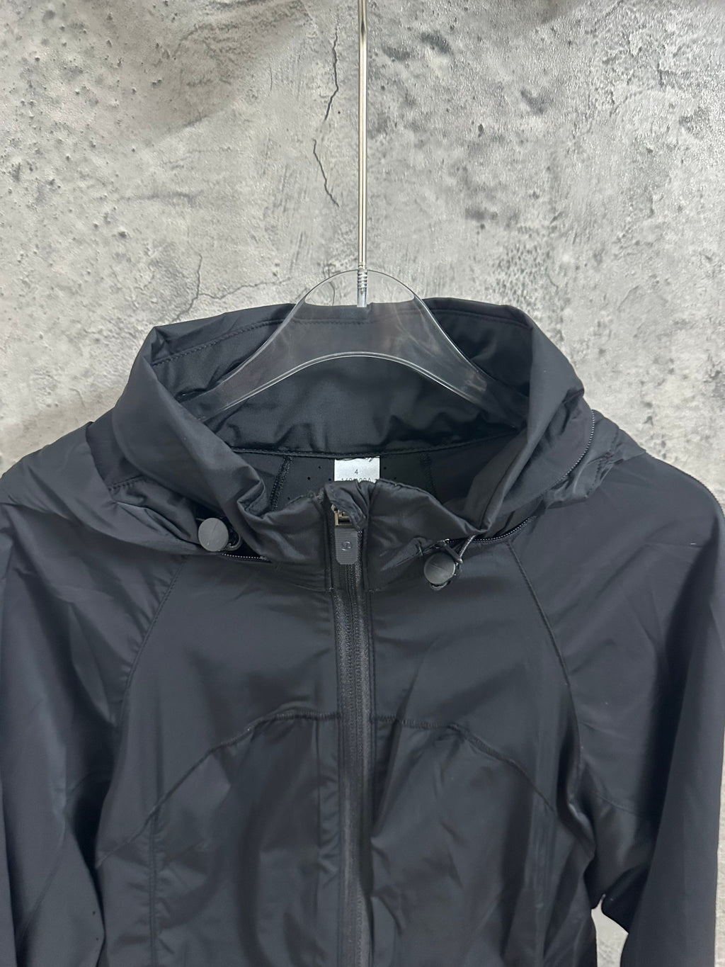 Hooded rain jacket chest close-up with front zipper and drawcord hood, dark color