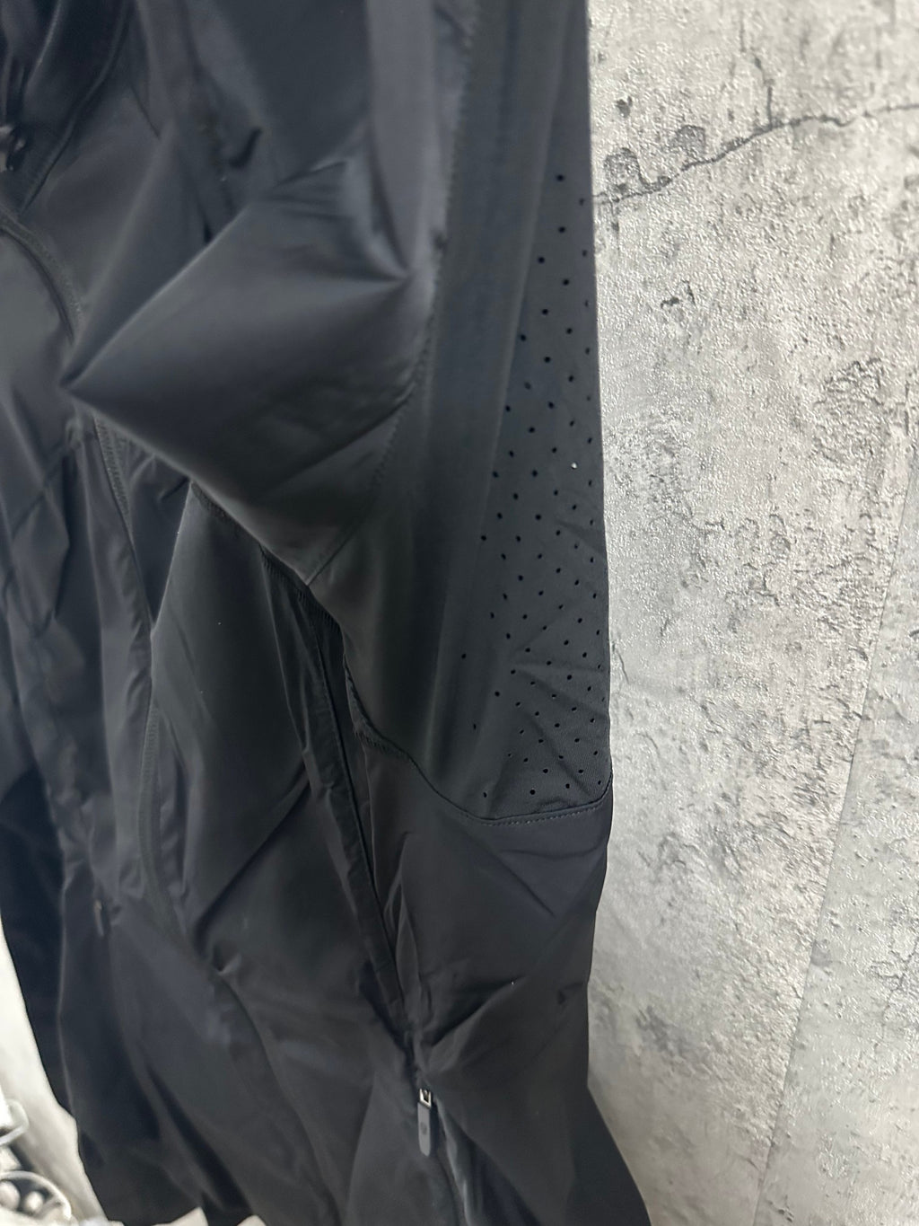 Hooded rain jacket sleeve and shoulder close-up with small ventilation holes, dark color