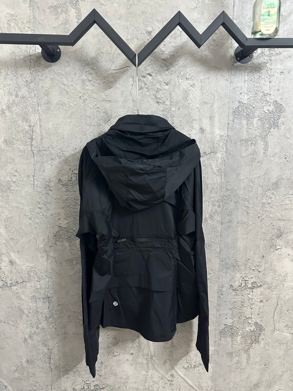 Hooded rain jacket back view with adjustable hem, dark color, long sleeves