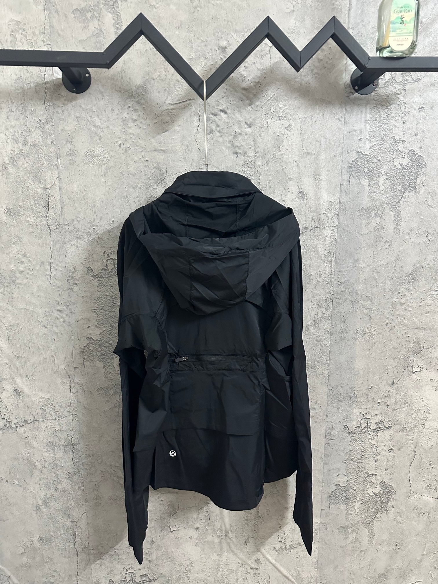 Hooded rain jacket back view with adjustable hem, dark color, long sleeves