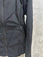 Hooded rain jacket side close-up with zipper pocket and seam details, dark color